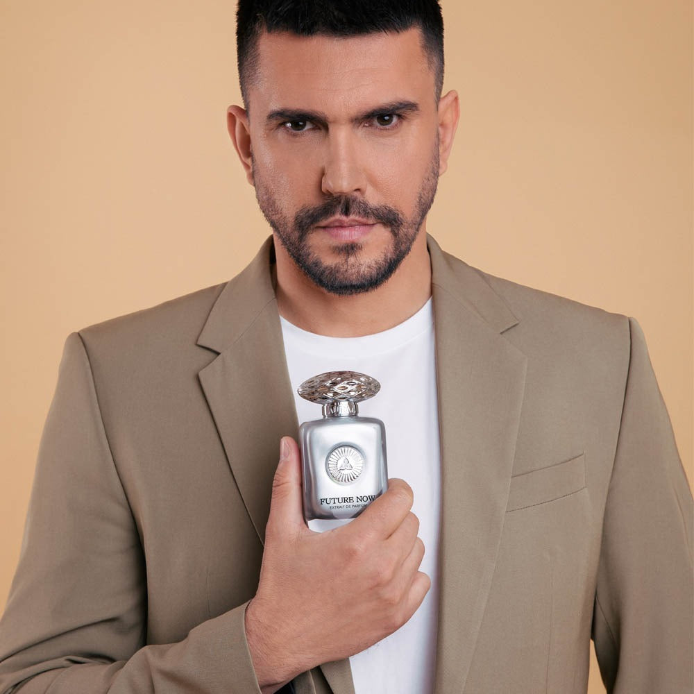 A man in a beige blazer holding a silver perfume bottle