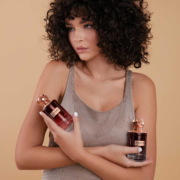 A women with curly hair wearing a silver dress holding two perfumes by Savia Exclusive