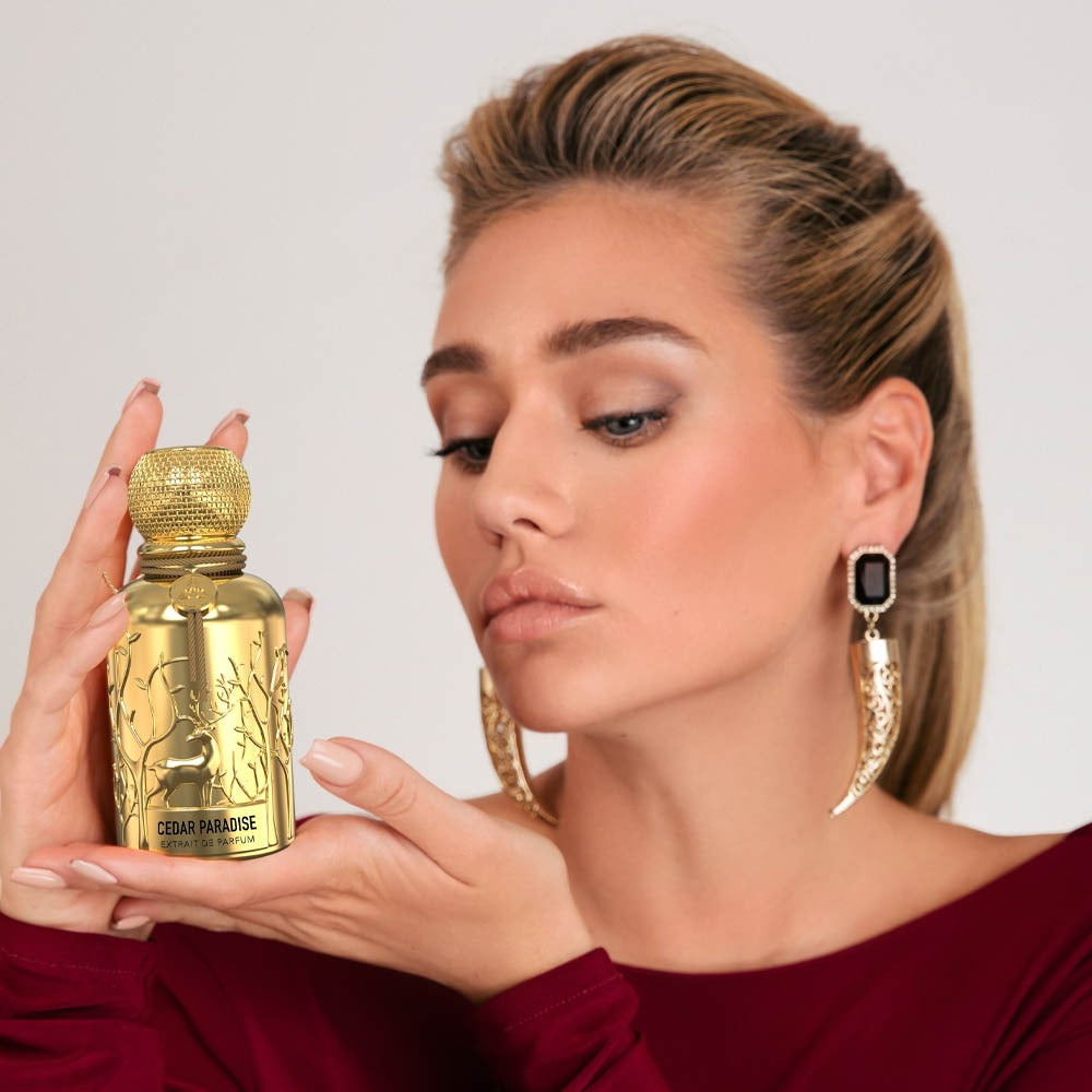 A woman wearing a maroon dress holding a golden Savia Exclusive perfume bottle