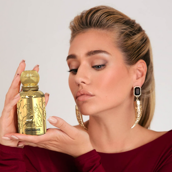 A woman wearing a maroon dress holding a golden Savia Exclusive perfume bottle