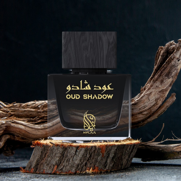 A grey & black perfume bottle from Nylaa by Savia Exclusive with a black cap placed on a brown oak platform with oak branches