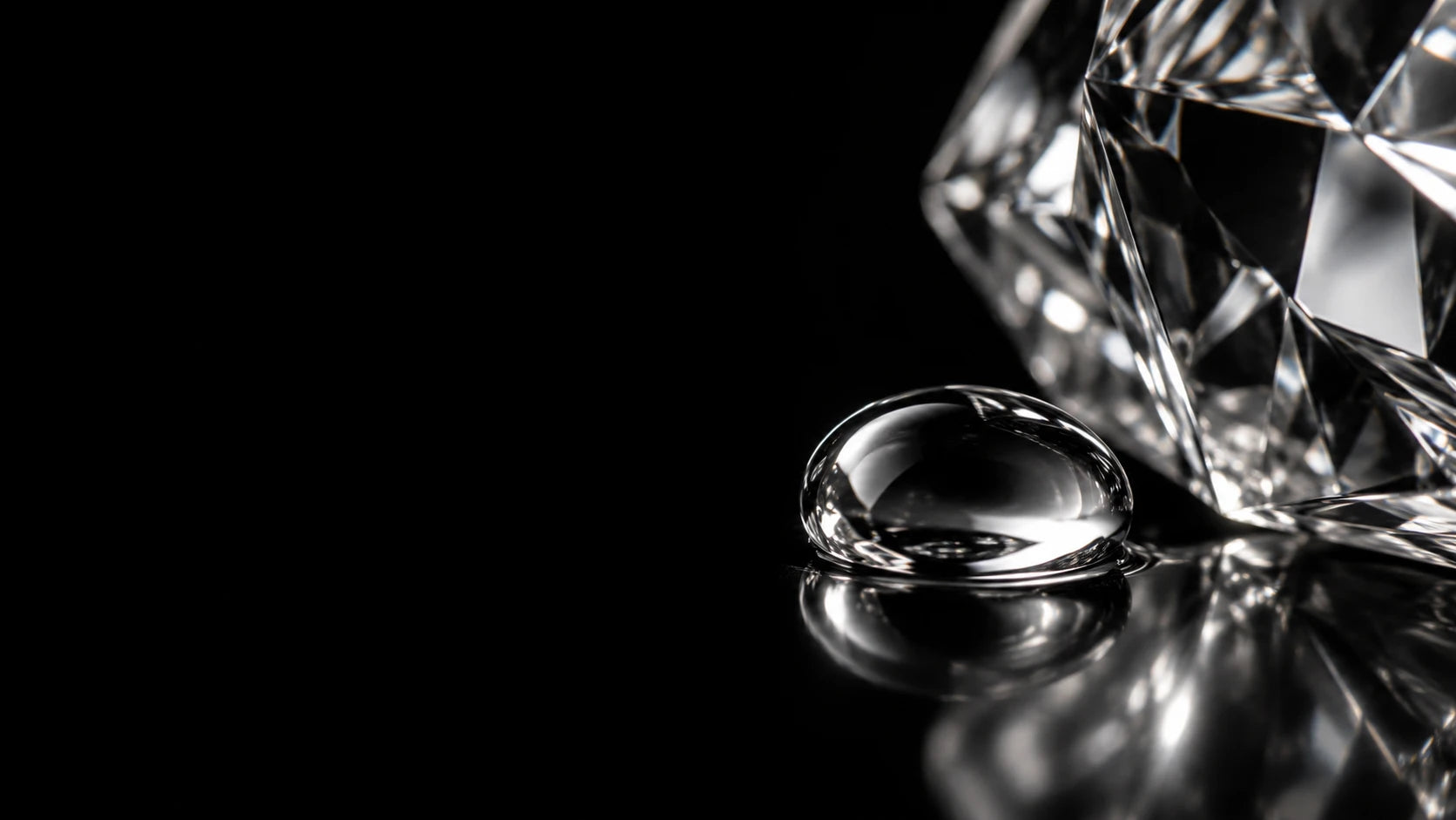 Macro photograph of clear crystal and a perfume droplet on black glass